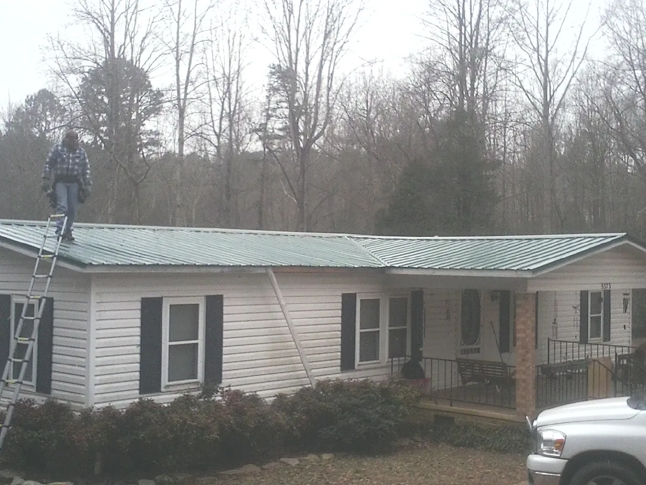 Worker on a ladder beside a new green metal roof on a ranch home in Marydel