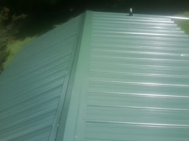 New green metal panels meeting at the ridge of a roof — Flat Roof Repair work by our crew in Marydel