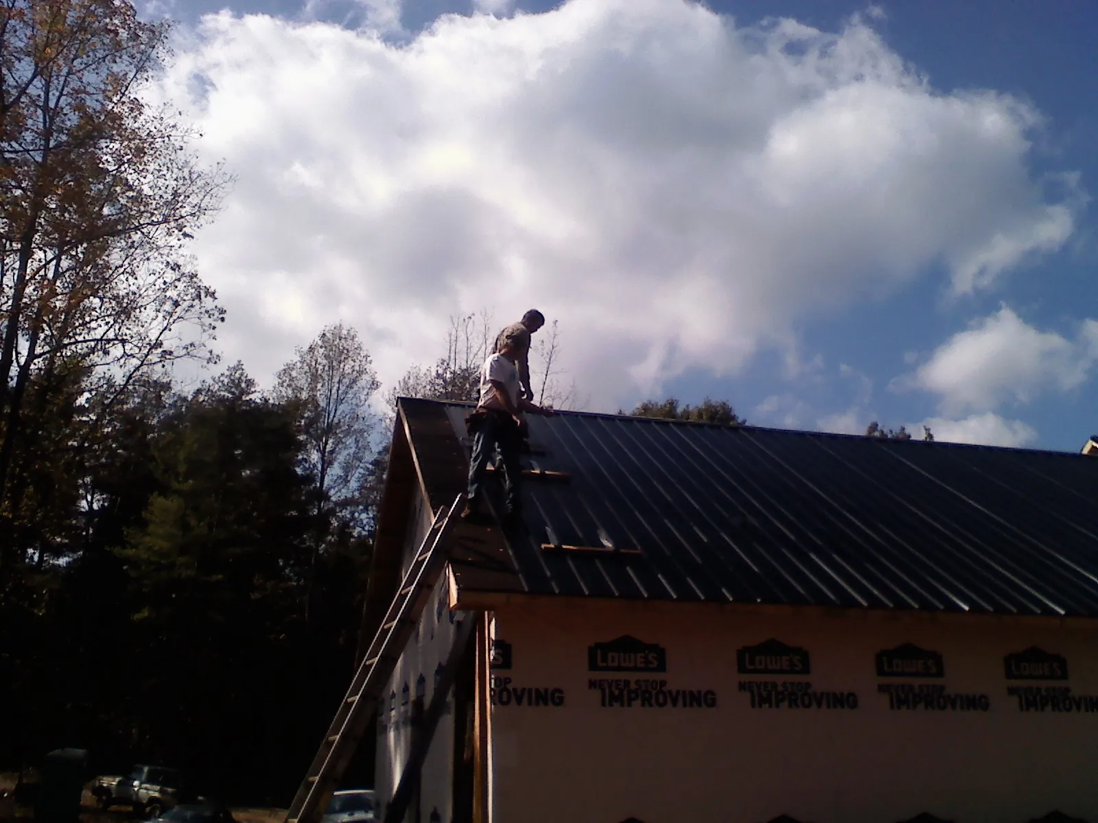 Roofer fastening dark metal panels high against a cloudy sky, from a Roof Inspection job in Marydel