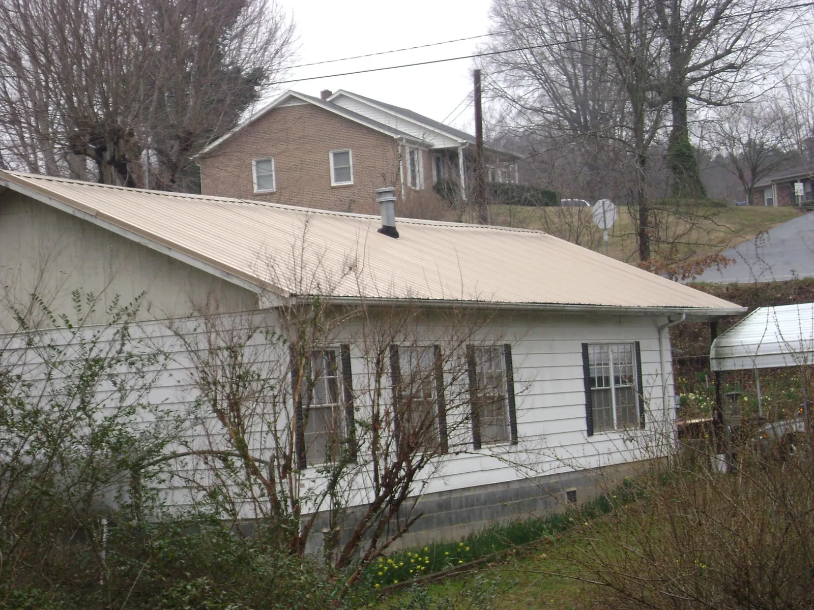 Tan metal roof on a white sided house set into a hillside — Commercial Roofing by Roofing Brothers in Marydel